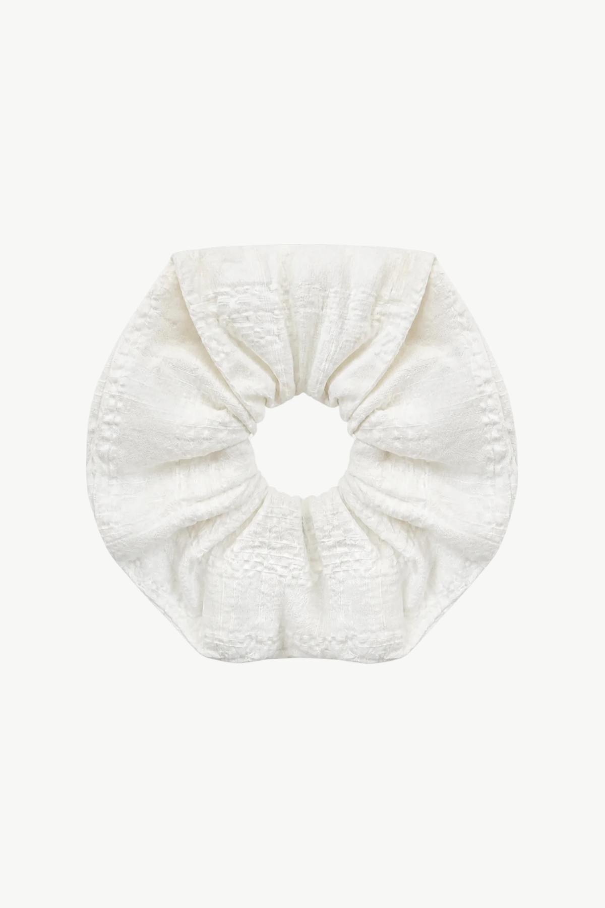 A single textured fabric scrunchie in a warm off-white or cream color, centered on a solid light gray background.