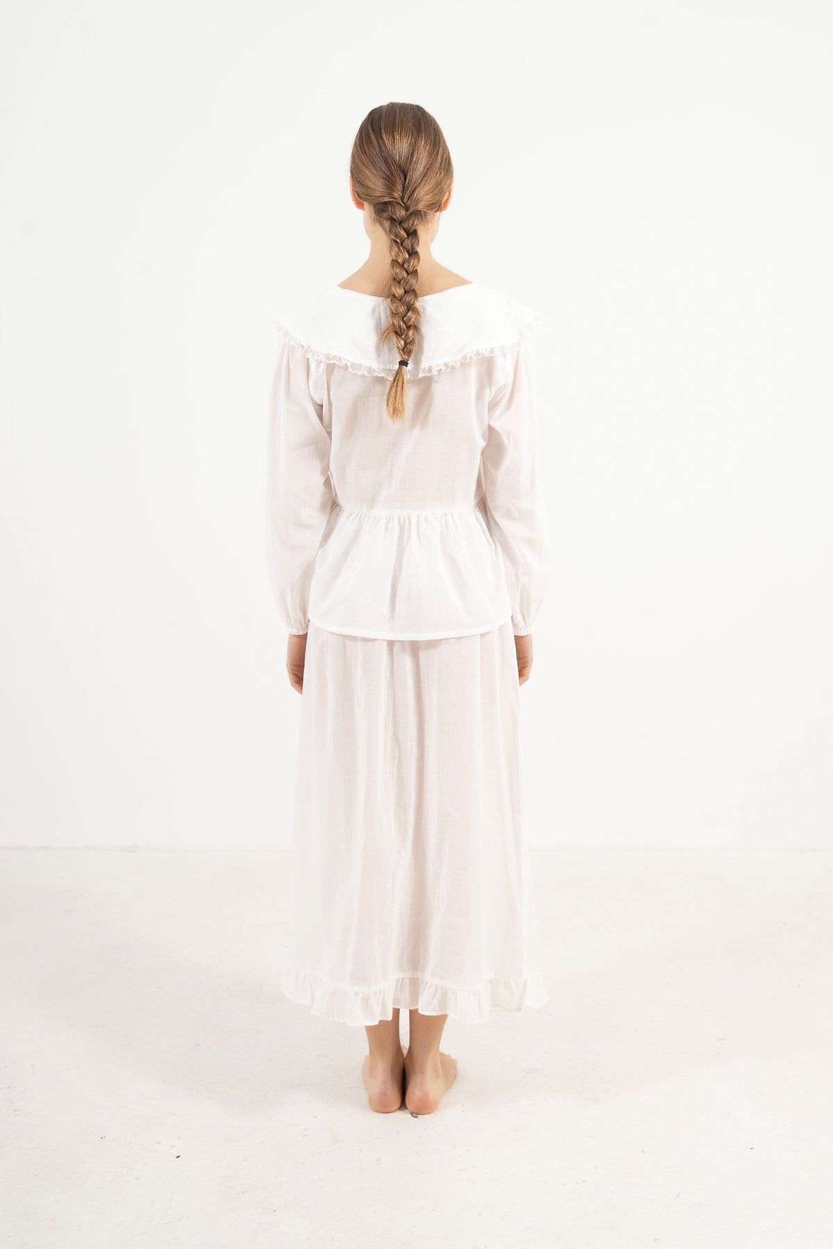 Back view of the timeless white cotton blouse on a model, capturing a sense of calm ease, understaded femininity, and clean design.