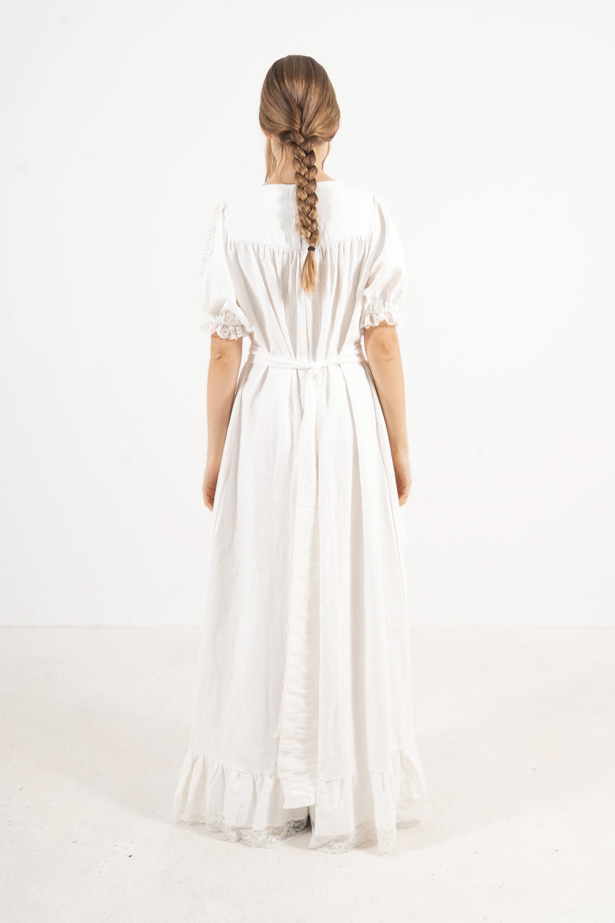 Back view of the timeless long white cotton dress on a model, capturing a soft world of ease inspired by air, movement, and calm days.