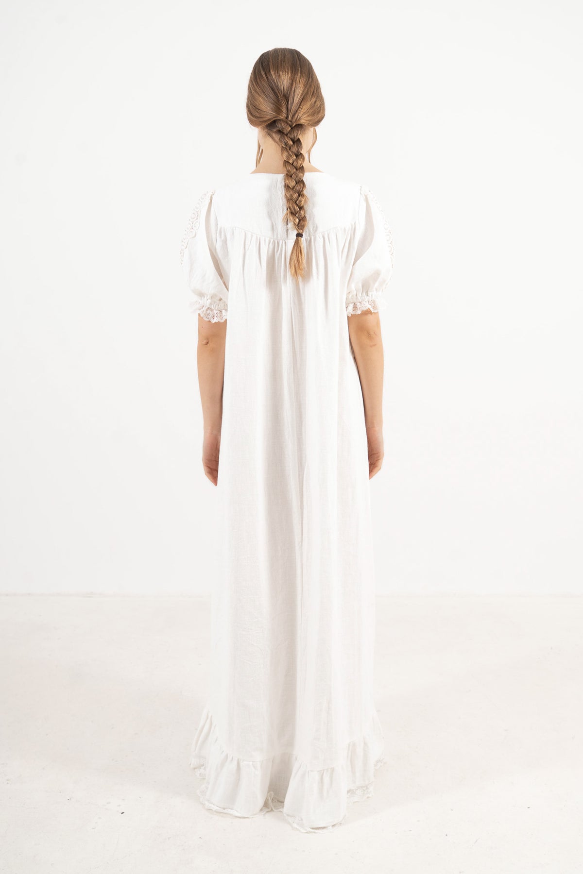 Back view of the timeless long white cotton dress on a model, capturing a soft world of ease inspired by air, movement, and calm days.
