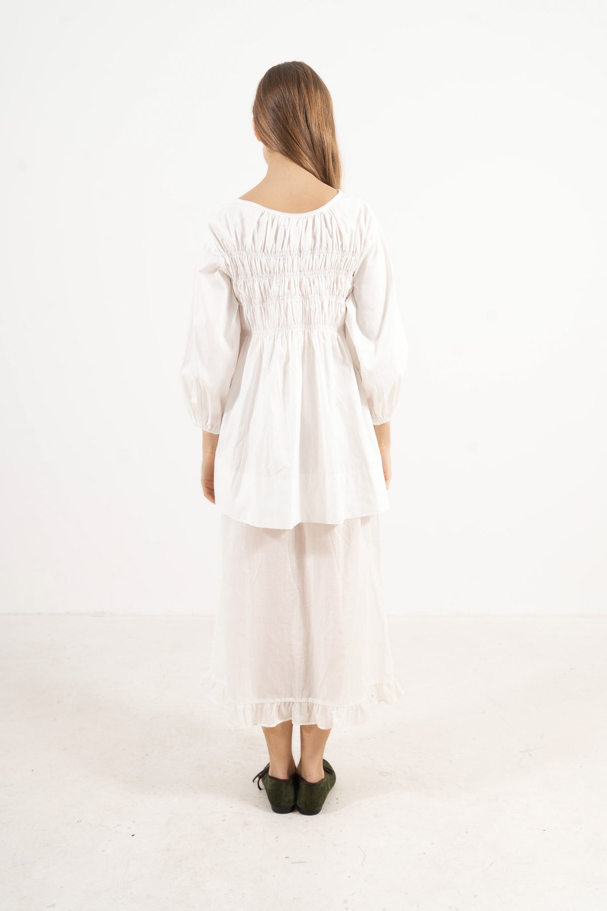 Back view of the timeless organic cotton blouse on a model, capturing the elegant heritage, calm ease, and seamless tailoring of the piece.