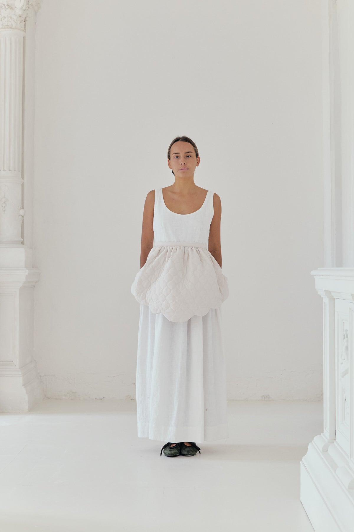 An elegant front view of the MOCHA Le Petit Tablier de Poésie mid apron dress, meticulously crafted from the finest pure cotton and draped beautifully upon a pristine white floor.