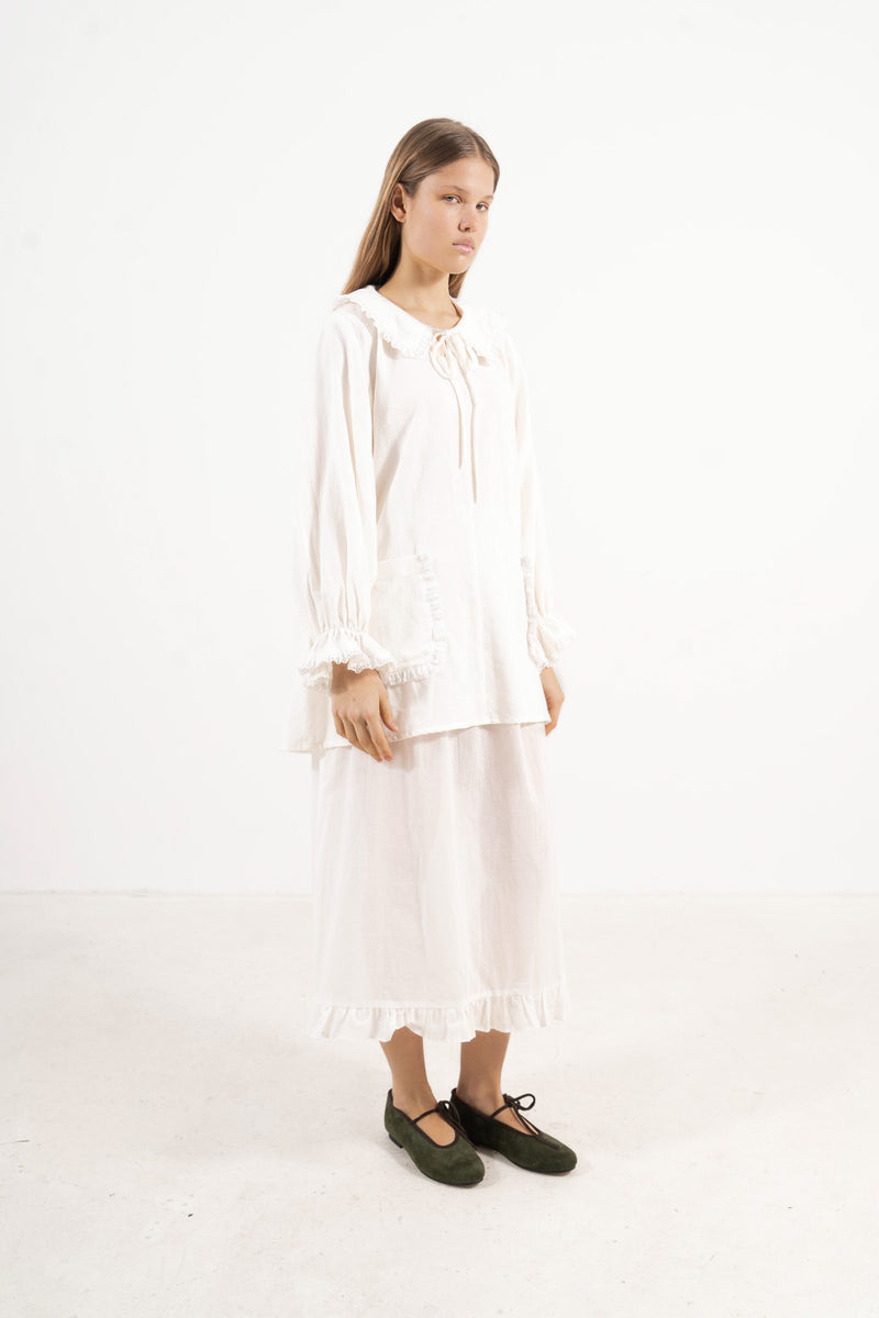Side lookbook capture of the white cotton tunic, emphasizing how the long sleeves and light fabric move with effortless grace.