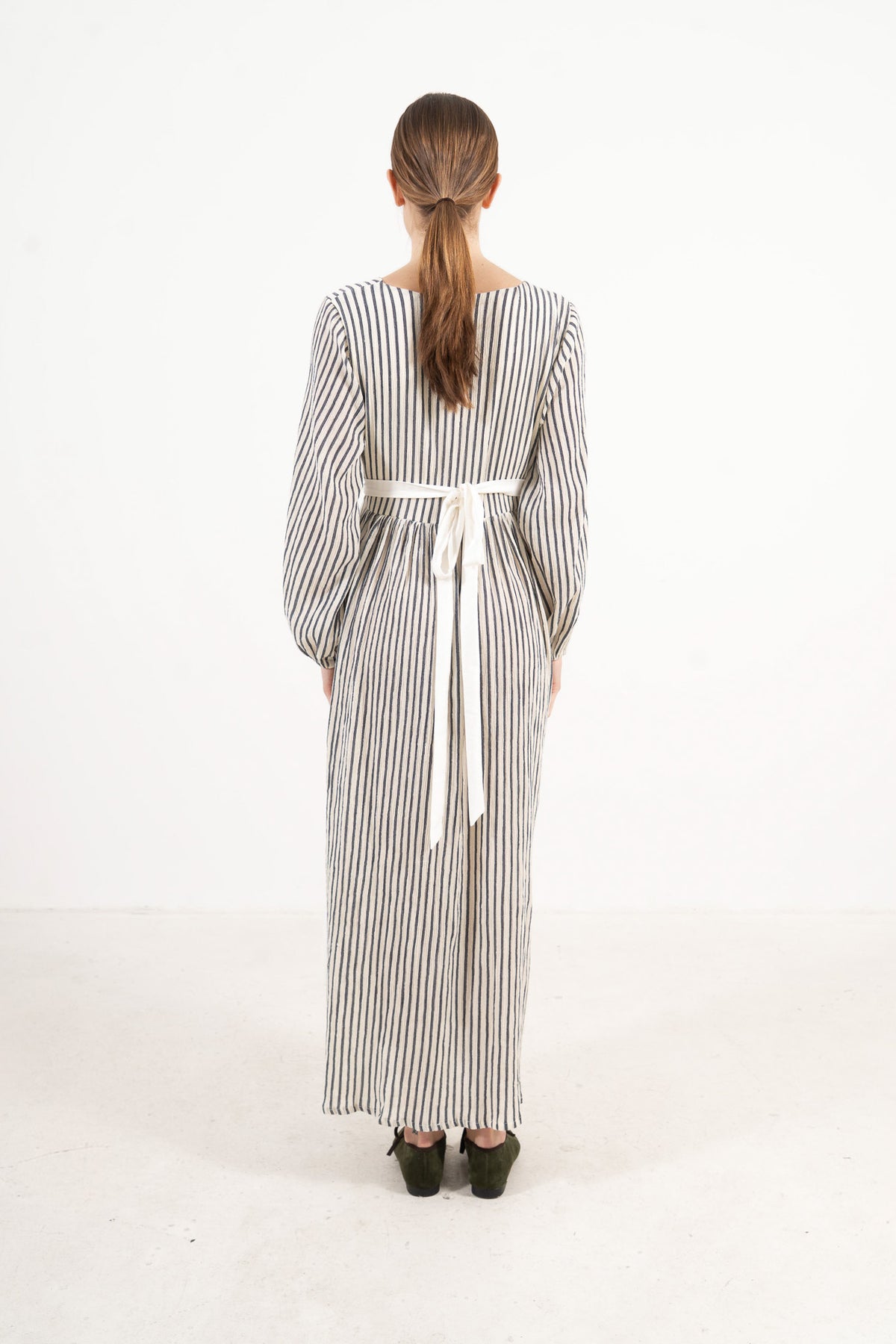 Back view of the long apron on a model, showcasing the delicate tie straps and the fine craftsmanship of the piece.