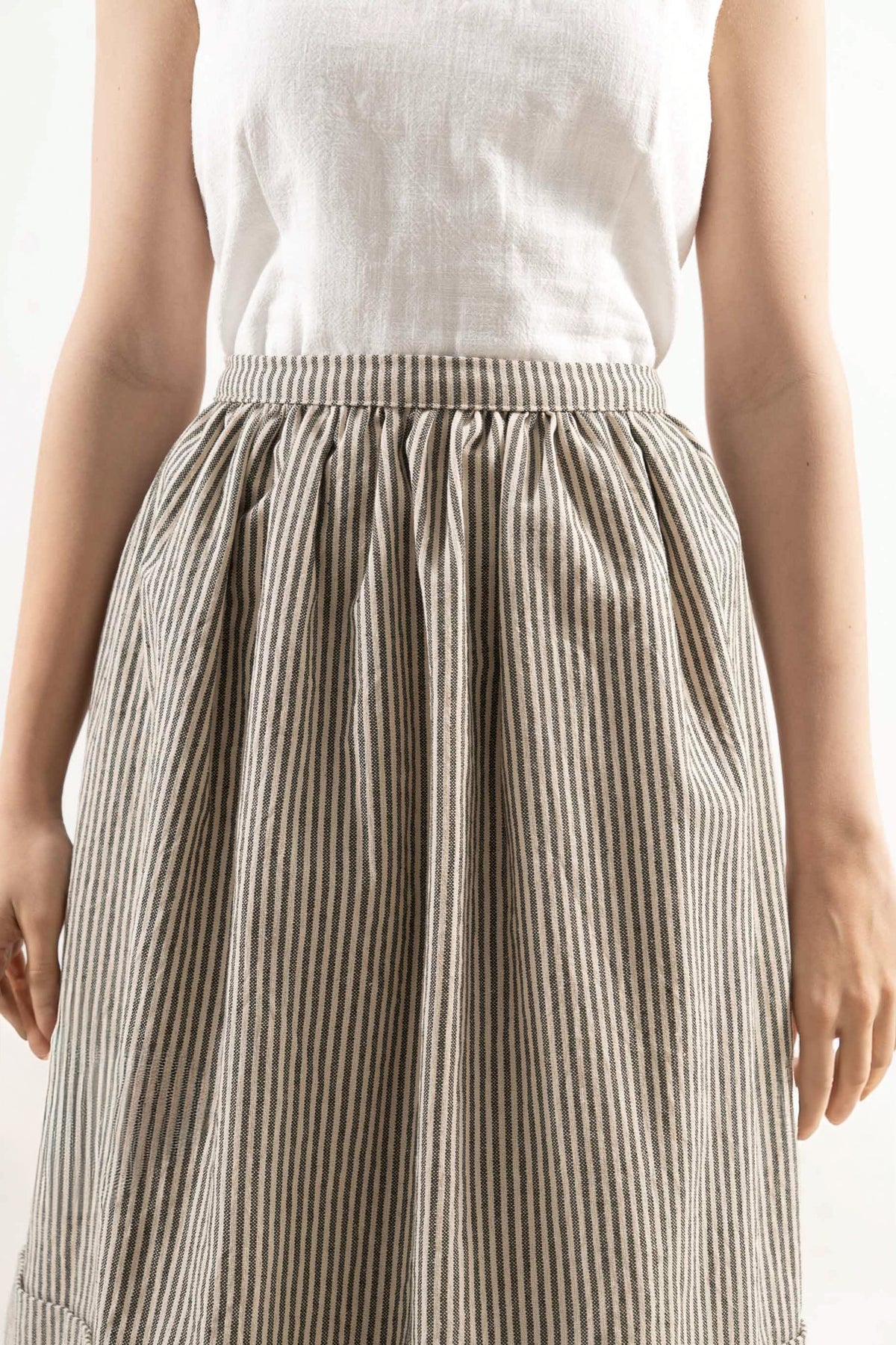 Close-up detail shot focusing on the delicate volants, fine stripe pattern, and premium cotton weave, celebrating the beauty of slow kitchen rituals.