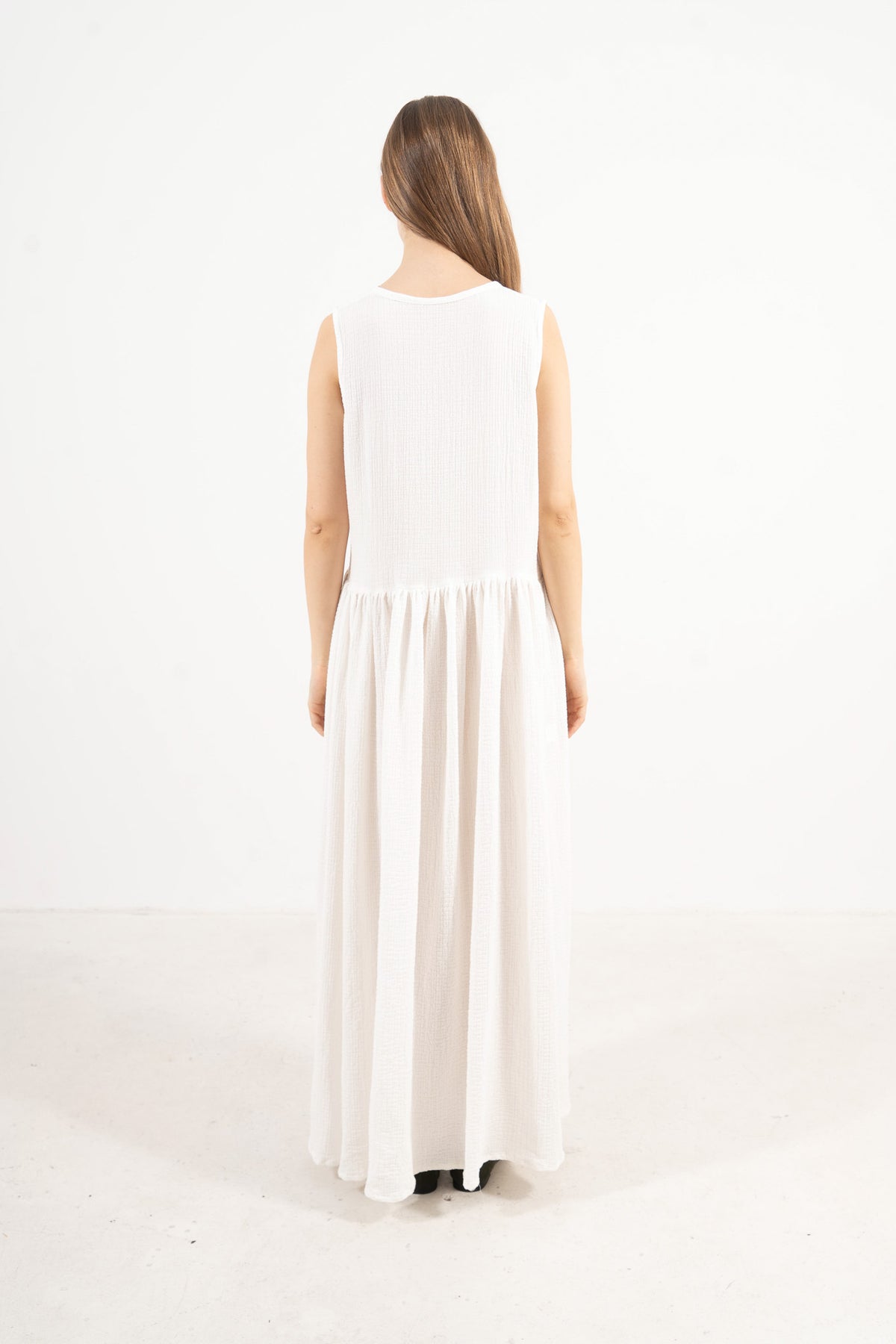 The refined back view of the MOCHA Nuage long dress in fine soft cotton, displaying a clean, understated silhouette laid flat on a polished white floor.