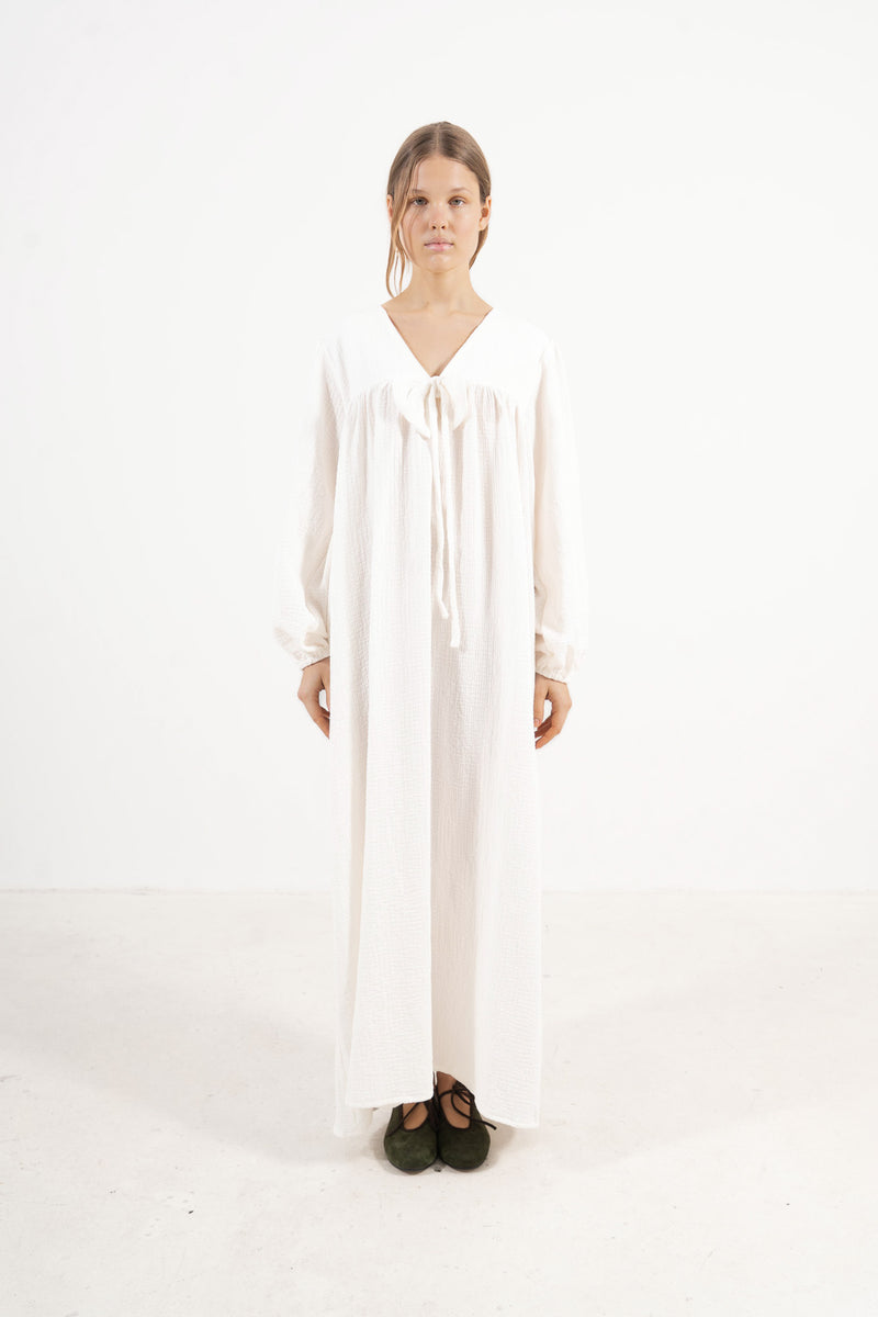 An elegant front view of the MOCHA Pearl Bow dress, meticulously crafted from the finest organic cotton and draped beautifully upon a pristine white floor.