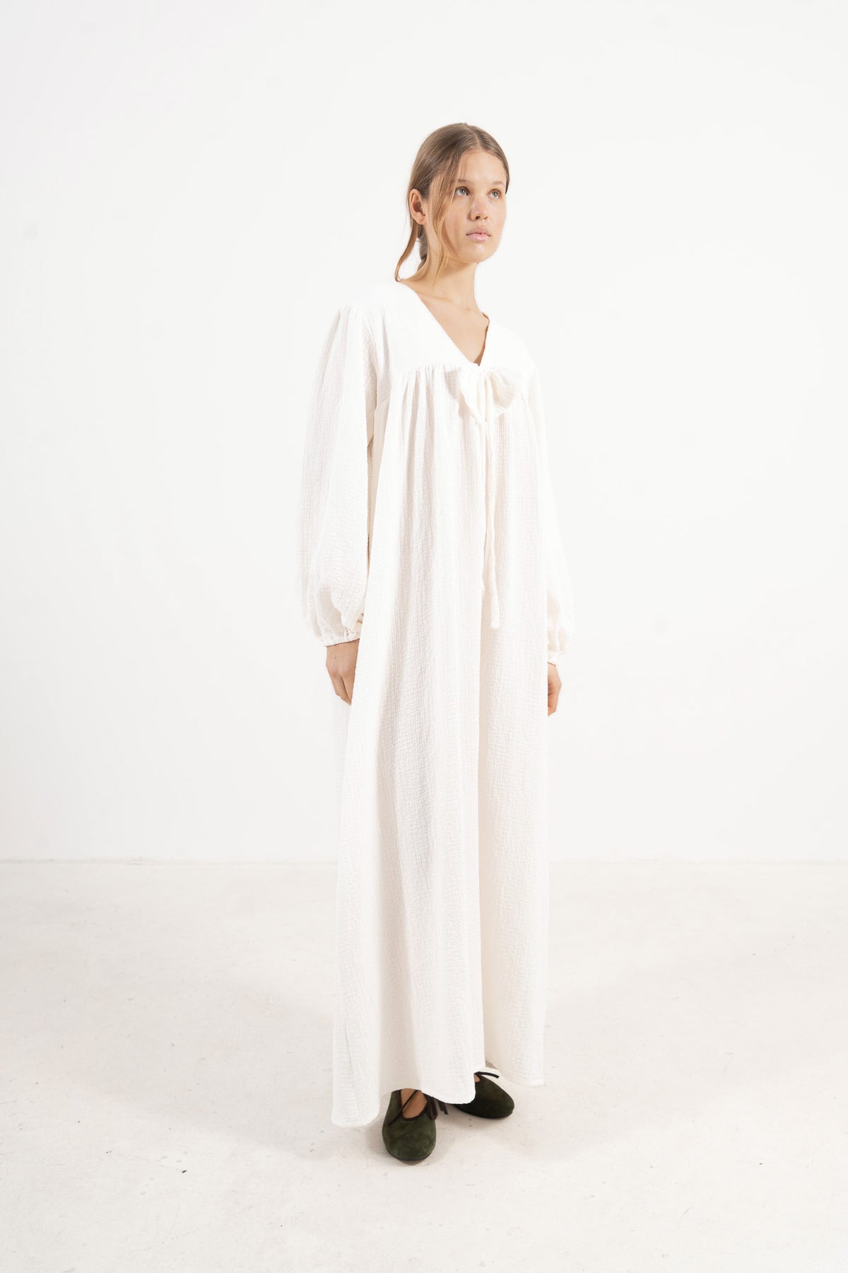 A sophisticated profile view of the standalone MOCHA Pearl Bow dress in pure cotton, revealing its graceful lines resting on a clean white surface.