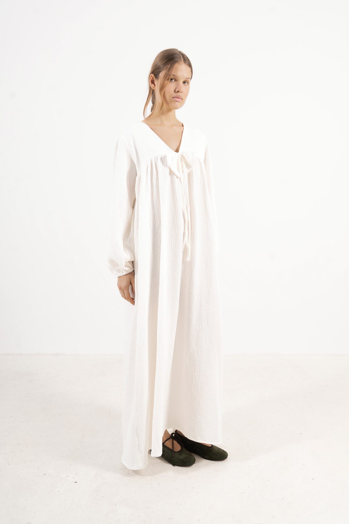 A poetic side angle view of the premium cotton MOCHA Pearl Bow dress, showcasing the gentle flow of its romantic long sleeves against a white backdrop.