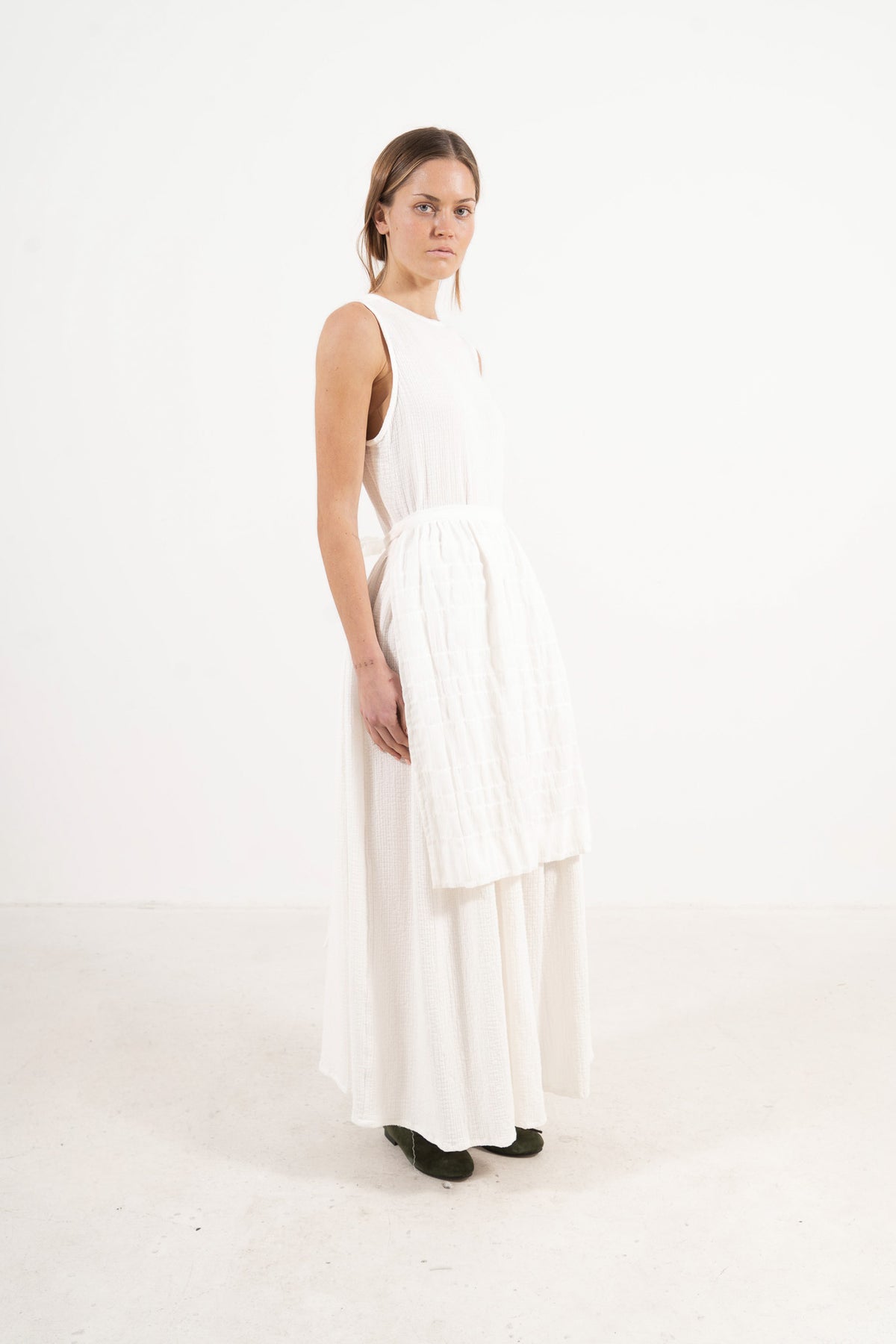 Side profile view of Le Tablier Mid Apron by MOCHA, capturing the delicate flow of the shoulder volants and the clean drape of the mid-length silhouette.