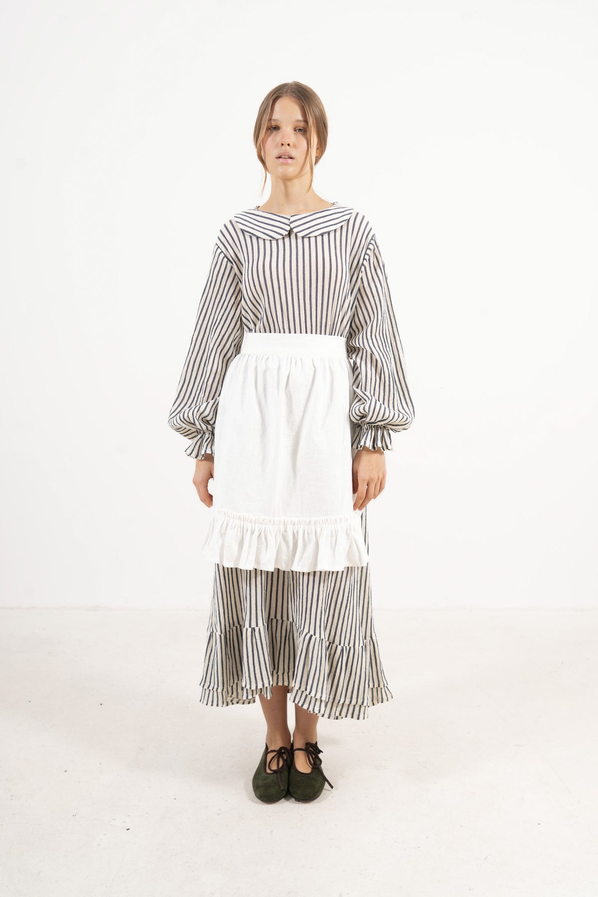 Woman wearing a black and white striped dress with a white apron on a white background