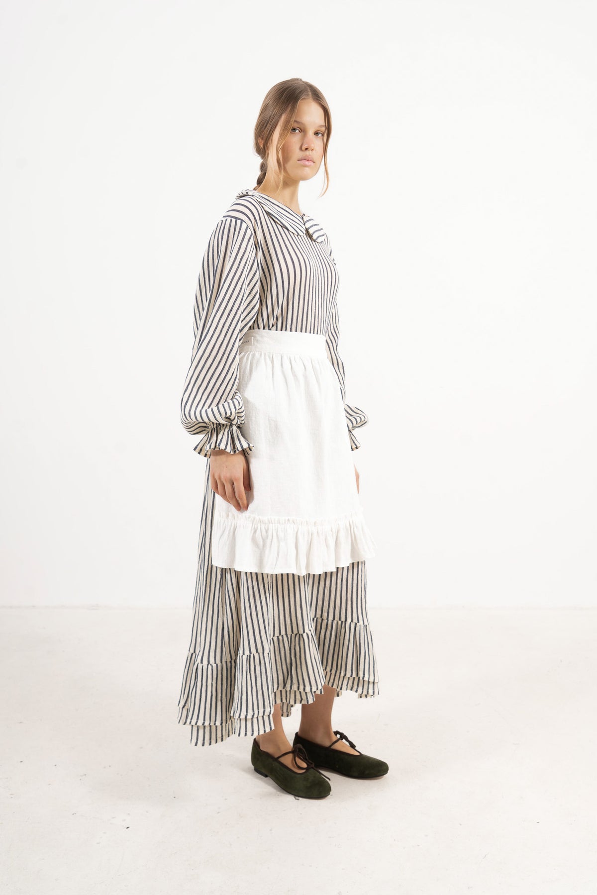 Woman wearing a black and white striped dress with a white apron on a white background